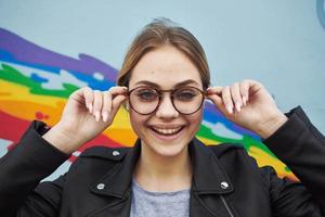 glücklich Frau im ein Leder Jacke und Brille in der Nähe von das mehrfarbig Graffiti auf das Mauer foto