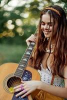 glücklich Hippie Frau mit ein Gitarre entspannend im Natur Sitzung auf ein Plaid lächelnd und genießen das Sicht. Lebensstil im Harmonie mit Natur und selbst foto