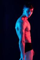 sexy Mann mit ein aufgepumpt Torso posieren auf ein dunkel Hintergrund Seite Aussicht und Neon- Licht foto