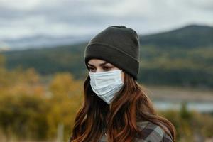 Frau im ein medizinisch Maske im das Berge in der Nähe von das Herbst Wald foto