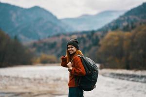 Frau im ein Hut mit ein Rucksack sind ruhen im das Berge im Natur in der Nähe von das Fluss foto