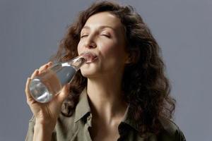 genossen glücklich lockig schön Frau im beiläufig khaki Grün Hemd halt Flasche trinken sauber Mineral Wasser posieren isoliert auf Über grau Blau Hintergrund. gesund Lebensstil. Wasser ist Leben Konzept. Kopieren Raum foto