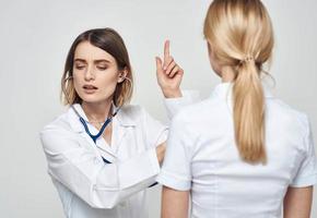 Arzt Frau im ein medizinisch Kleid mit ein Stethoskop kommuniziert mit ein geduldig zurück Aussicht foto