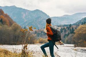 Frau im ein Jeans Sweatshirt mit ein Rucksack sich ausruhen im das Berge in der Nähe von das Fluss im Natur foto