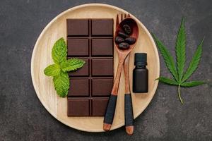 Cannabisblatt mit dunkler Schokolade, Pflanzenblättern und Holzutensilien auf einem dunklen Betonhintergrund foto