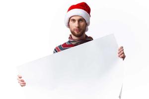 gut aussehend Mann im ein Weihnachten Hut mit Weiß Attrappe, Lehrmodell, Simulation Poster Weihnachten Licht Hintergrund foto