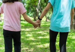 zwei Schwester halten Hände im das Park im warm Frühling Tag. glücklich Freundschaft Familie Konzept. foto