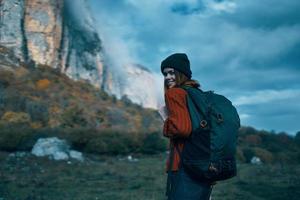 Frau Reisender im ein Sweatshirt mit ein Rucksack auf ihr zurück im Herbst im das Berge auf Natur und Himmel Wolken foto