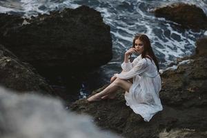 barfuß Frau im Weiß Kleid sitzt auf ein Cliff Natur oben Aussicht unverändert foto