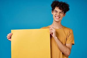 emotional Mann mit lockig Haar Gelb Poster im das Hände von Kopieren Raum foto