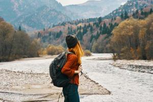 Frau im Sweatshirt mit ein Rucksack sich ausruhen im das Berge in der Nähe von das Fluss im Herbst im Natur und hoch Bäume Modell- foto