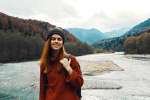 schön Frau im ein Sweatshirt mit ein Rucksack im das Berge in der Nähe von das Fluss im Natur Porträt foto