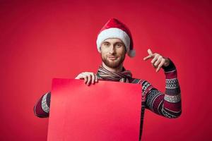 emotional Mann im ein Santa Hut halten ein Banner Urlaub rot Hintergrund foto