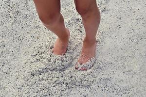 das Beine von ein Junge Gehen auf hell, Feuchtigkeit Sand beim das Kante von ein Wasser Reservoir während Ferien foto