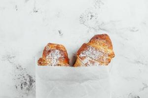 zwei frisch Croissants im ein Papier Tasche auf ein Marmor Hintergrund, oben Aussicht foto