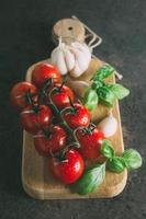 organisch Produkt - - Tomate, Basilikum, Knoblauch auf Schneiden Tafel auf dunkel browm Beton Stein Hintergrund foto