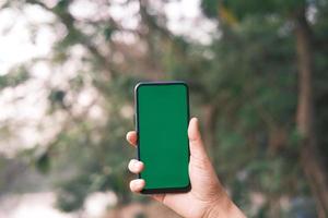 Mann hält Telefon draußen mit grünem Bildschirm foto