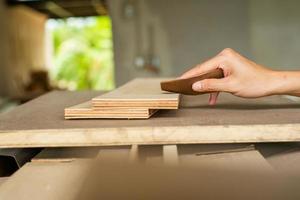 Selektiver Fokus auf eine Hand des Tischlers, der Sandpapier hält und die Holzoberfläche schrubbt foto