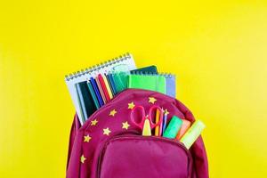 zurück zu Schule Konzept. rot Rucksack mit anders Schreibwaren auf Gelb Hintergrund. oben Aussicht foto