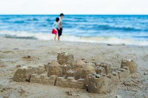 Sandburg gebaut unter Verwendung der Form mit Menschen, die auf dem Strand im Hintergrund gehen foto