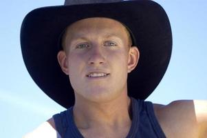 ein jung, blond Cowboy ist abgebildet im Nahaufnahme, mit das nur Hintergrund Sein das Himmel. foto