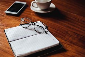 Gläser auf einem Notizbuch mit Kaffee und einem Telefon foto