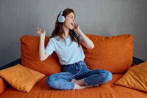 heiter Frau auf das Orange Sofa Hören zu Musik- mit Kopfhörer Technologien foto