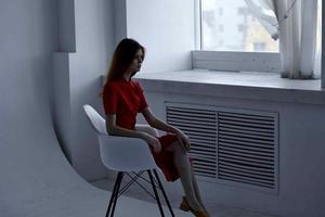 schön Frau im rot Kleid Sitzung in der Nähe von das Fenster elegant Stil foto