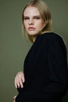 Porträt von ein atemberaubend elegant Mädchen im ein schwarz passen posieren beruflich auf ein Grün Hintergrund im das Studio. das Konzept von Werbung zum Designer Marken foto