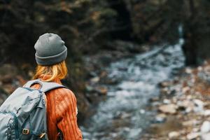 Frau in der Nähe von das Fluss im das Berge mit ein Rucksack auf ihr Schultern sind ruhen im das Herbst Wald foto