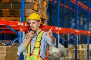 lagerarbeiter, der in der fabriklagerindustrie arbeitet und funkkommunikation nutzt, vorarbeiter in hardhat-sicherheitsweste mit funkgerät, das im logistikzentrum arbeitet foto