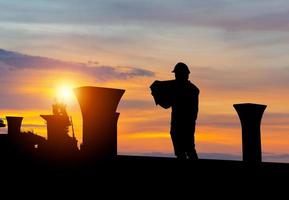 Silhouette von Ingenieur Mann Überprüfung Projekt beim Gebäude Seite? ˅ Hintergrund, Infrastruktur Konstruktion Seite? ˅ beim Sonnenuntergang im Abend Zeit foto