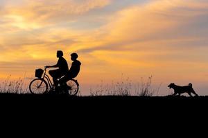 Silhouette von Mann und Freund Reiten Fahrrad mit ihr Hund beim Sonnenuntergang Abend Himmel Hintergrund foto