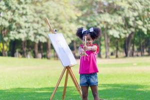 heiter Kind Mädchen Gemälde auf Segeltuch im das Garten, glücklich Kind Mädchen Zeichnung ein Bild draußen foto