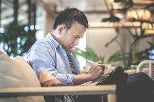 asiatisch Mann mit ein Tablette Zeichnung ein Grafik auf Tablette im ein modern Kaffee Geschäft, Technologie im verwenden Konzepte foto