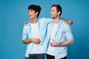 jung Männer im identisch Hemden umarmen auf ein Blau Hintergrund Beste freunde Spaß foto