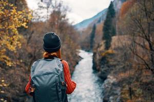 Frau Wanderer mit ein Rucksack auf ihr zurück in der Nähe von ein Berg Fluss im Natur, zurück Aussicht foto