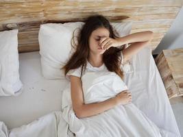 Frau Lügen im Bett unter das Abdeckungen hält ihr Hand auf ihr Gesicht Morgen foto