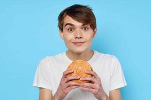 Mann Essen Hamburger im Weiß T-Shirt Diät Essen Lebensstil Blau Hintergrund foto