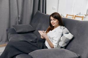 Frau mit Handy, Mobiltelefon Telefon Sitzung auf das Couch Innere Zimmer foto