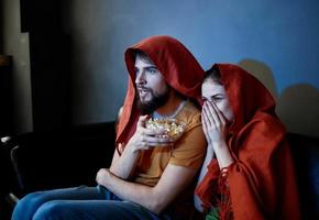 ein Mann und ein Frau mit ein rot Plaid auf ihr Köpfe sind Sitzung auf das Sofa im Vorderseite von das Fernseher drinnen foto