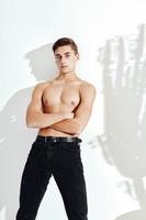 ein Mann mit ein aufgepumpt Torso auf ein Licht Hintergrund im schwarz Hose Verbreitung seine Beine zu das Seiten foto