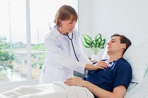 das Arzt ist Prüfung das geduldig im das Krankenhaus. kaukasisch weiblich Arzt reden zu männlich geduldig Lügen im Krankenhaus Bett. foto