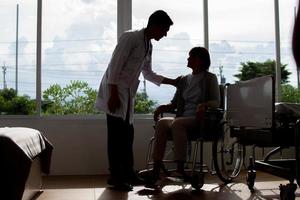 kaukasisch Mann Arzt ist Prüfung das weiblich älter geduldig im Rollstuhl das Krankenhaus. foto