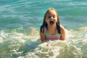 ein wenig Mädchen im ein Badeanzug schwimmt fröhlich im das Meer auf ein warm Sommer- sonnig Tag foto
