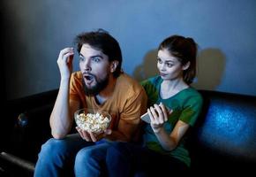 ein Mann und ein erschrocken Frau Aufpassen ein Film im das Abend auf das Couch mit ein Teller von popcor foto