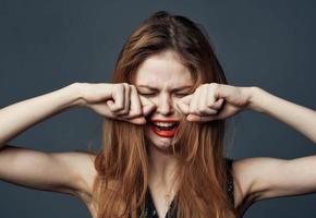 Frau mit rot Lippen Weinen auf grau Hintergrund und Hände in der Nähe von Gesicht abgeschnitten Aussicht foto