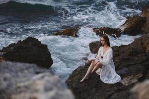 Frau im Weiß Kleid sitzt auf ein Stein in der Nähe von das Ozean Wellen Reise Natur foto