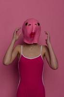 Frau Stehen im ein Rosa Fisch Maske auf ihr Kopf, ein provokativ verrückt Halloween sehen, Rosa Hintergrund im das Studio foto