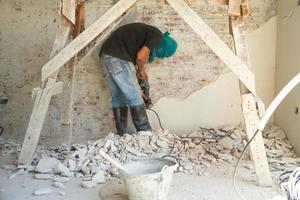 Rückenporträt eines Arbeiters, der die Zementoberfläche mit der Bohrmaschine von der Wand entfernt foto